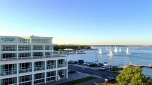 Waterfront hotel exterior with Chesapeake Bay view, modern architecture, sailboats on water, calm morning light, residential waterfront setting, no signage or text visible