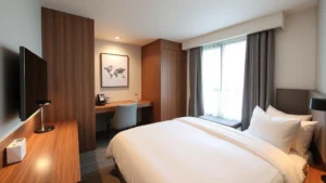 Modern mid-range hotel room with Japanese minimalist design, comfortable bed with white linens, wooden desk, compact but well-organized space, warm neutral lighting, clean and contemporary furnishings, professional business hotel aesthetic