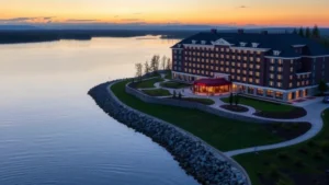 Serene waterfront view of a modern hotel overlooking Seneca Lake at sunset, with manicured grounds and peaceful water reflection, no signage visible
