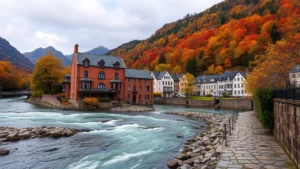 Charming brick hotel building nestled beside flowing river with mountain backdrop, autumn foliage visible on surrounding hills, peaceful waterfront setting with stone pathways
