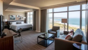 Modern hotel suite interior with contemporary furnishings, neutral tones, comfortable seating area overlooking coastal Southern California landscape, professional hospitality setting