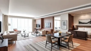 Modern spacious two-bedroom hotel suite interior with separate living room, dining area, and contemporary furniture in neutral tones, natural lighting from large windows