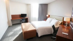 Modern hotel room with bed, desk workspace, and contemporary furnishings at an airport hotel, clean and well-lit natural light from window