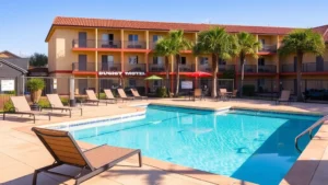 Outdoor swimming pool at a budget motel with clear blue water, lounge chairs, and palm trees, daytime sunny setting, residential hotel building in background