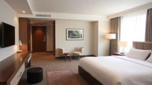 Modern hotel room interior with queen bed, neutral color palette, comfortable seating area, clean contemporary design, natural lighting from window