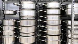 Professional stainless steel hotel pans stacked neatly in a commercial kitchen storage area, showing various pan depths and sizes organized on metal shelving racks