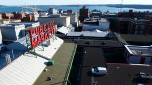 Aerial view of Pike Place Market rooftop with vendor stalls and Seattle waterfront visible in background, daytime, natural lighting