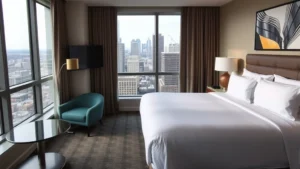 Modern hotel room interior with comfortable king bed, contemporary furniture, city skyline visible through window, Philadelphia downtown architecture in background